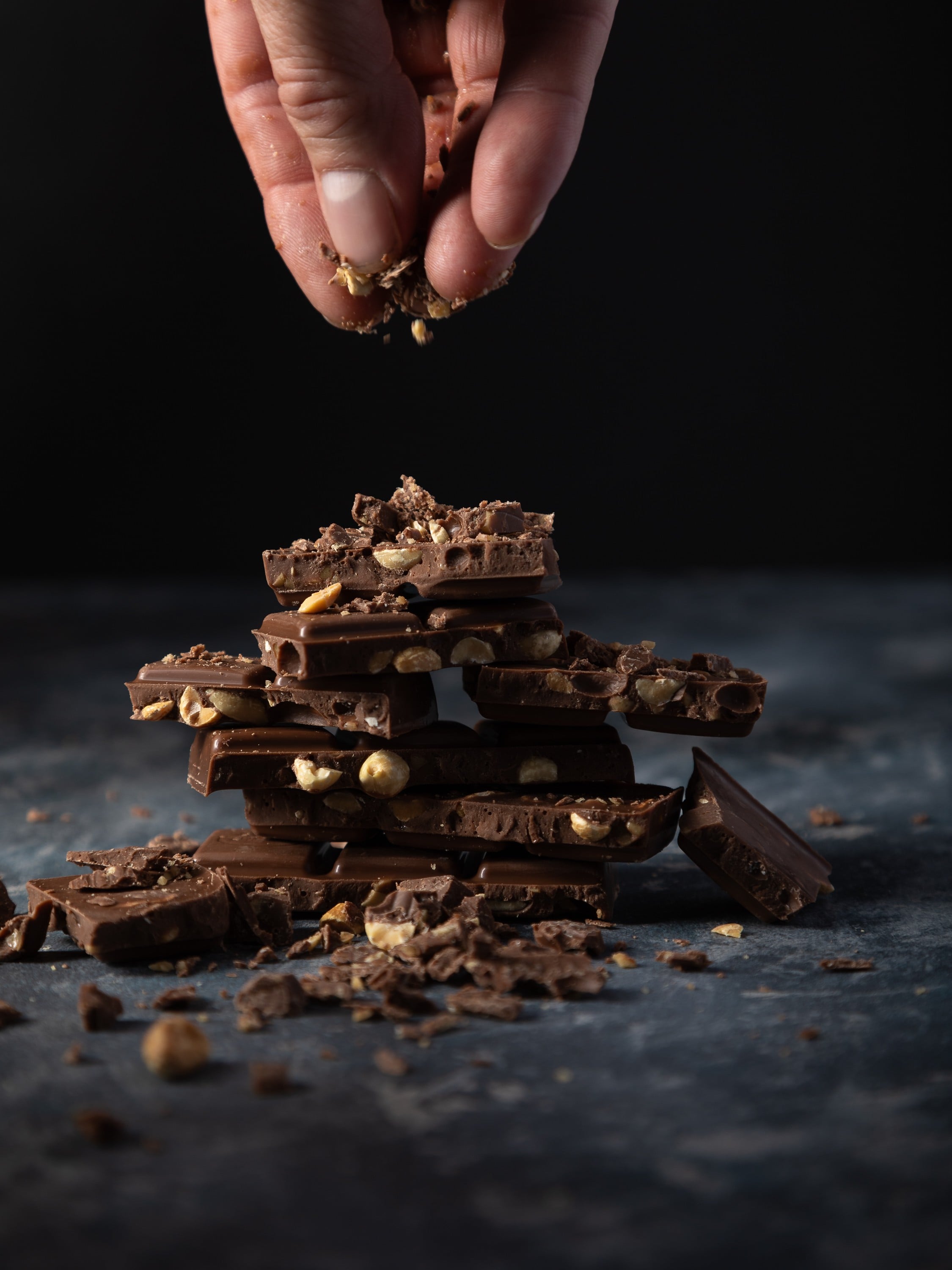 Broken chocolate pieces sprinkled with chocolate crumbs for food photography image. in a dark moody atmosphere.